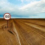Expansive desert road with a visible 100 speed limit sign and cloudy sky.